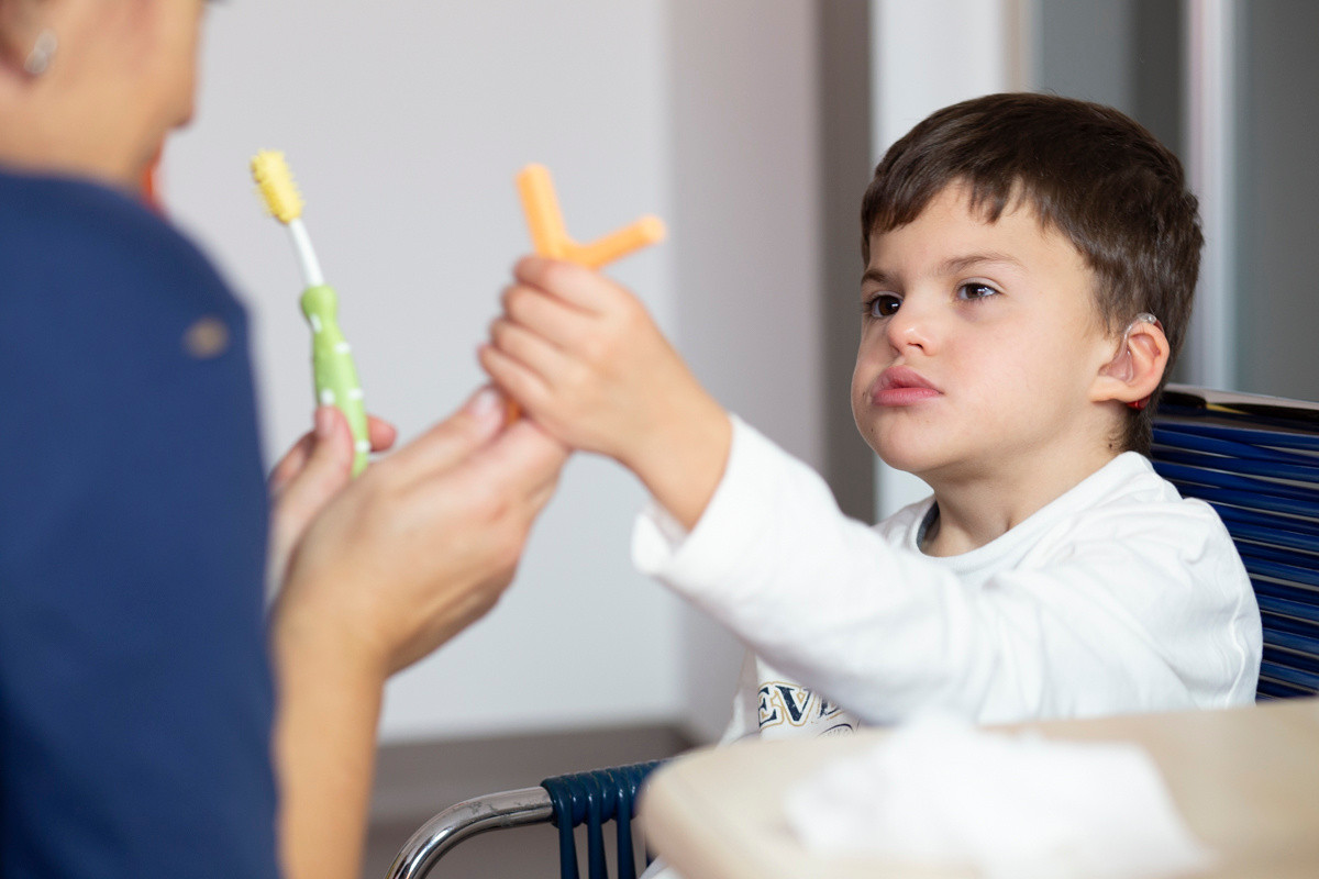 Agostino, bambino seguito al Centro di Osimo, sceglie uno dei due oggetti che l'educatrice gli sta mostrando per la sua prossima attività
