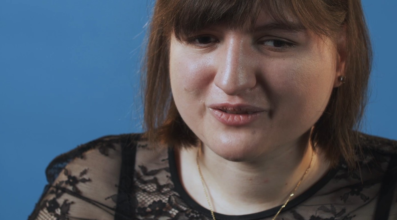 Foto in primo piano di Giona durante le riprese di un video. E' vestita elegantemente di nero e sorride. 