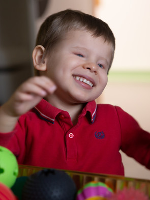 Matteo, bambino di 4 anni ospite del Centro Diagnostico, sorride davanti a una cesta piena di palline dalle forme diverse per la stimolazione tattile.