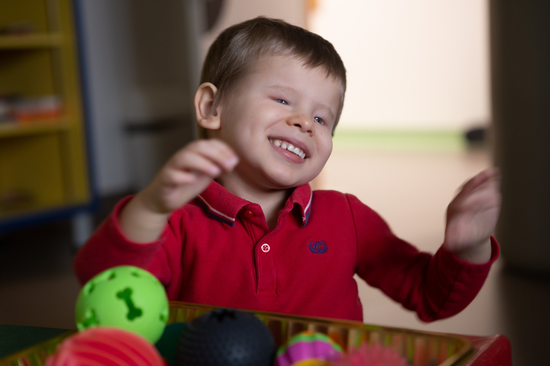 Matteo, bambino di 4 anni ospite del Centro Diagnostico, sorride davanti a una cesta piena di palline dalle forme diverse per la stimolazione tattile.