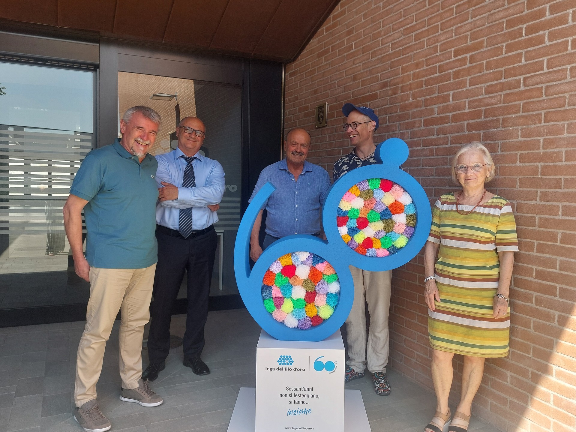 Foto di una visita istituzionale presso la Lega del Filo d’Oro. Alcune persone posano accanto all’installazione celebrativa dei 60 anni dell’associazione, all’ingresso della struttura, in occasione di un incontro ufficiale.