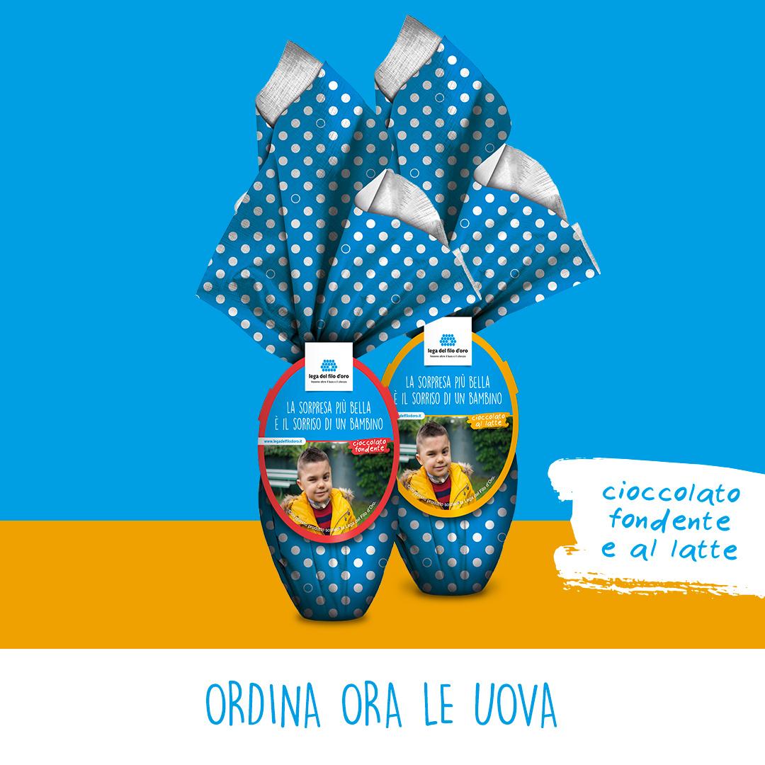 Su uno sfondo colorato azzurro e arancione, ci sono due uova di pasqua. Confezionate con una carta a pois azzurra e bianca, sono una al latte e l'altra al cioccolato.