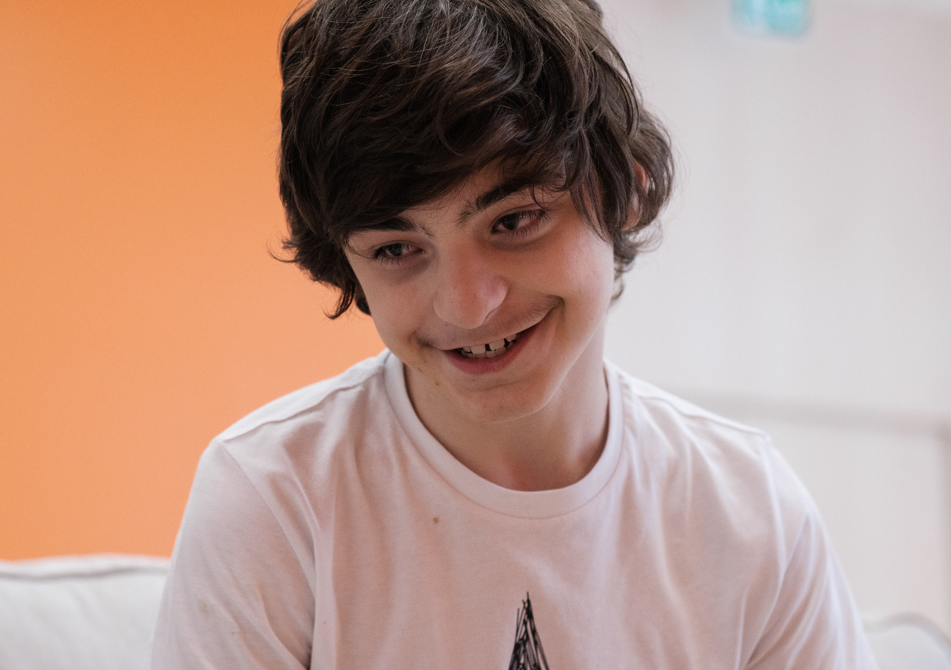 Francesco, un utente adolescente della Lega del Filo d'Oro che sorride seduto su un divano bianco