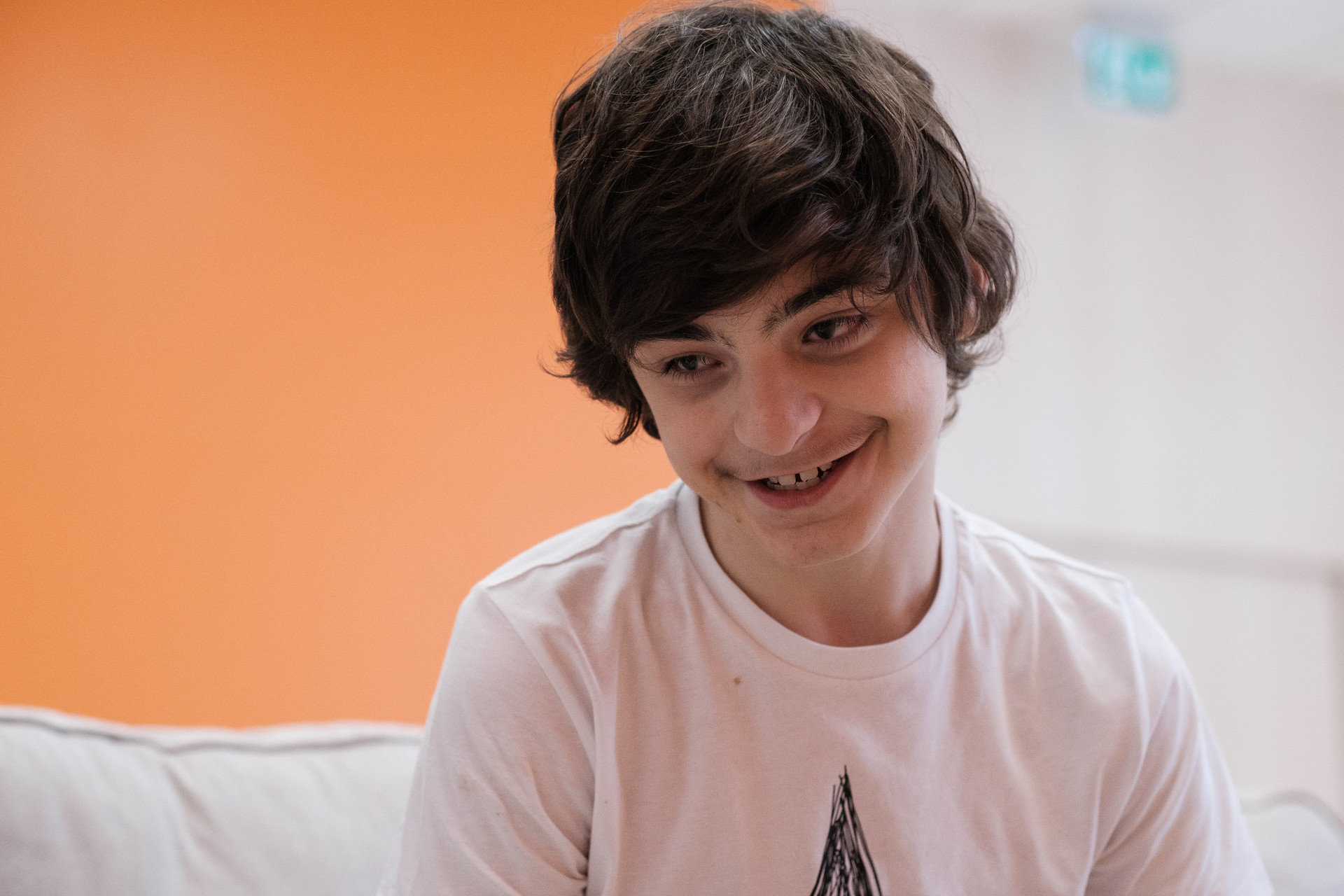 Francesco, un utente adolescente della Lega del Filo d'Oro che sorride seduto su un divano bianco 