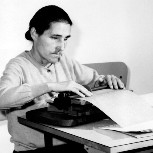 Sabina Santilli, fondatrice della Lega del Filo d'Oro, alla sua scrivania impegnata alla scrittura in dattilobraille. L'immagine è in bianco e nero.