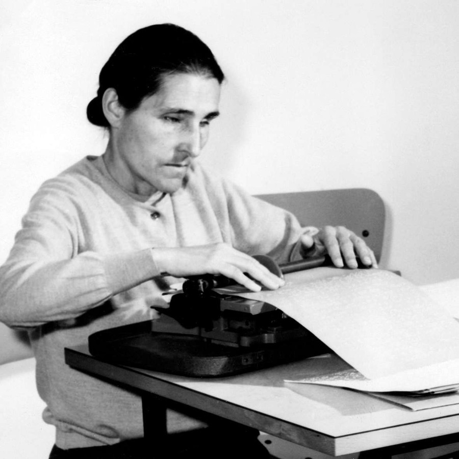 Sabina Santilli, fondatrice della Lega del Filo d'Oro, alla sua scrivania impegnata alla scrittura in dattilobraille. L'immagine è in bianco e nero.