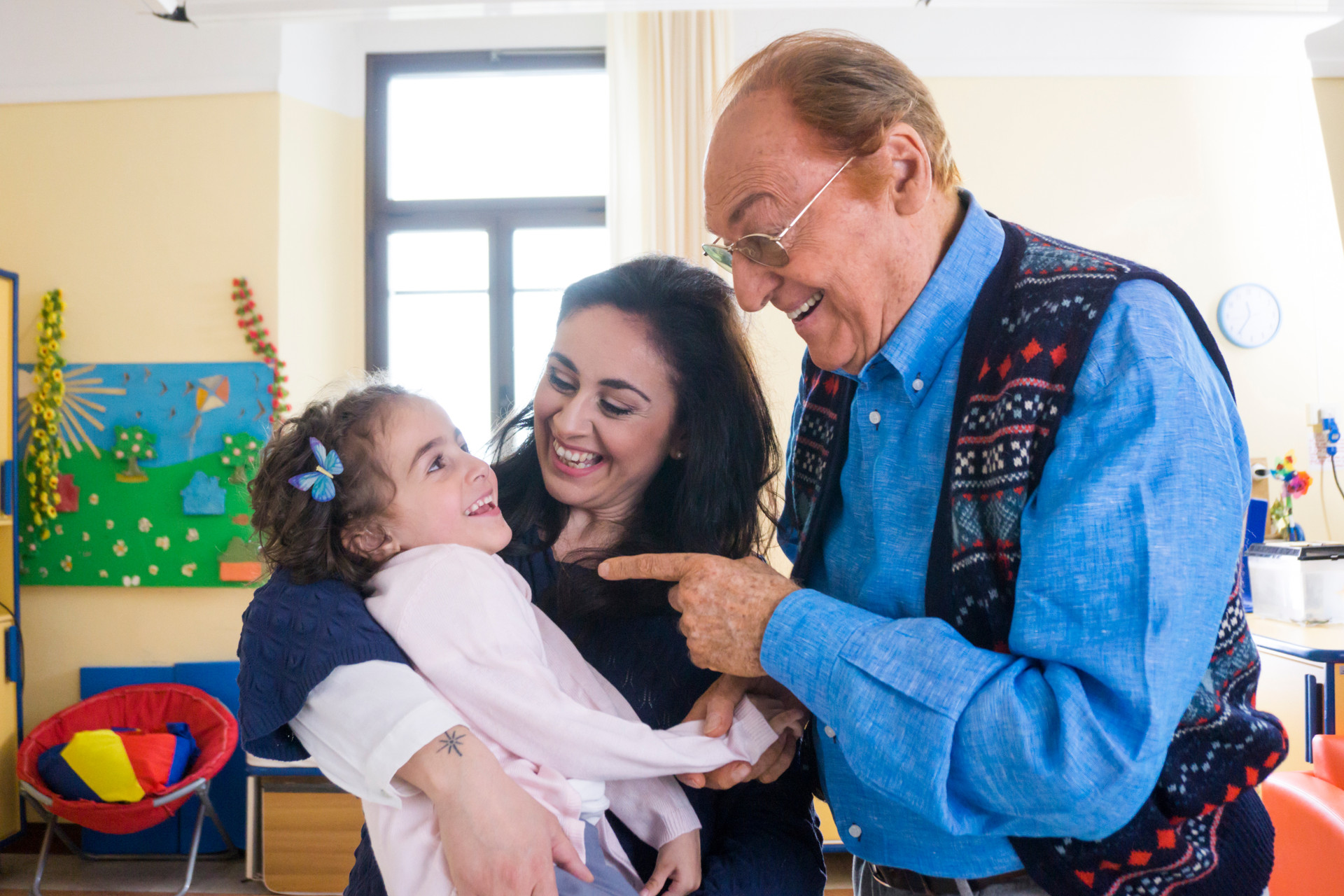 Immagine della campagna 5x1000: Renzo Arbore parla sorridendo con la piccola Sofia e la sua mamma