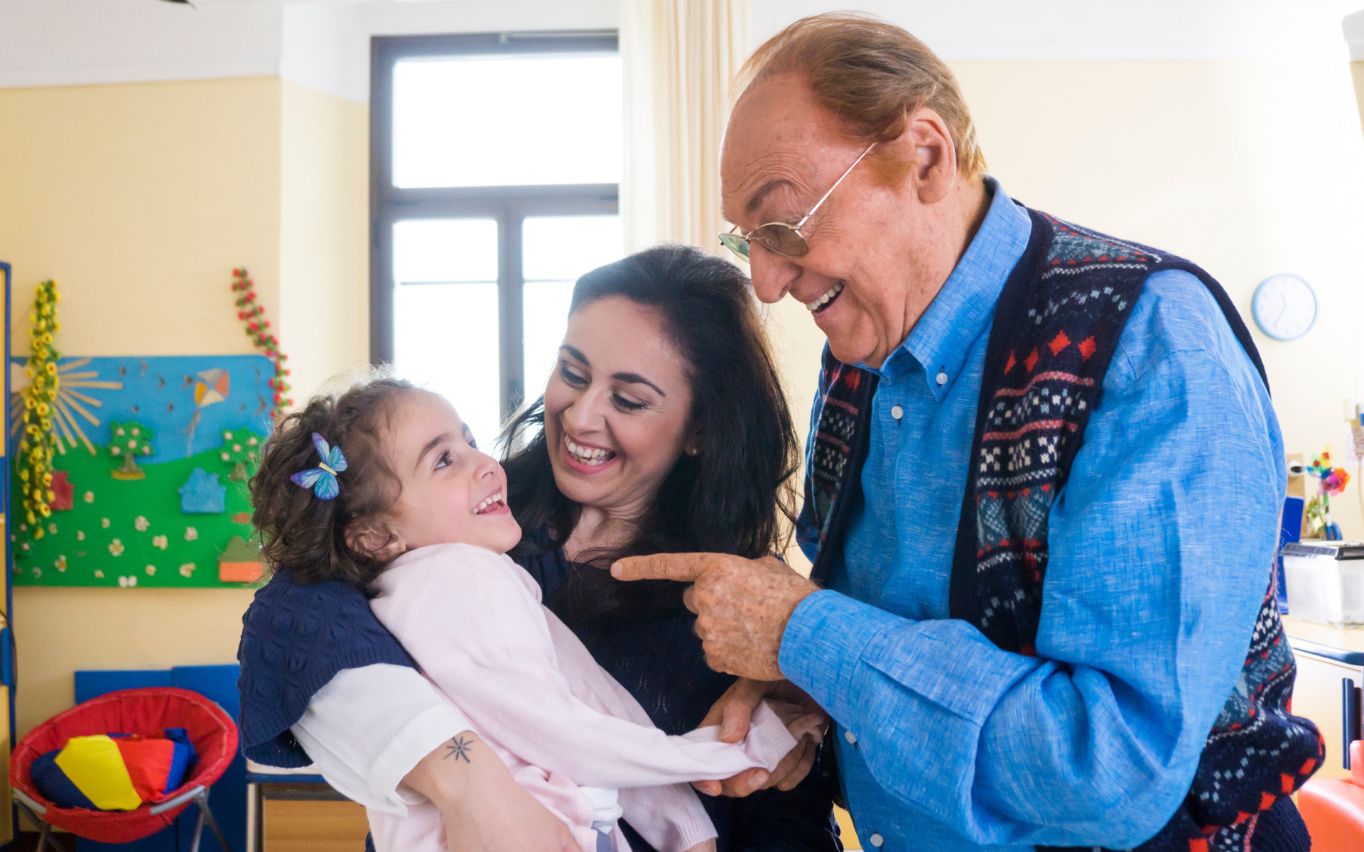 Immagine della campagna 5x1000: Renzo Arbore parla sorridendo con la piccola Sofia e la sua mamma