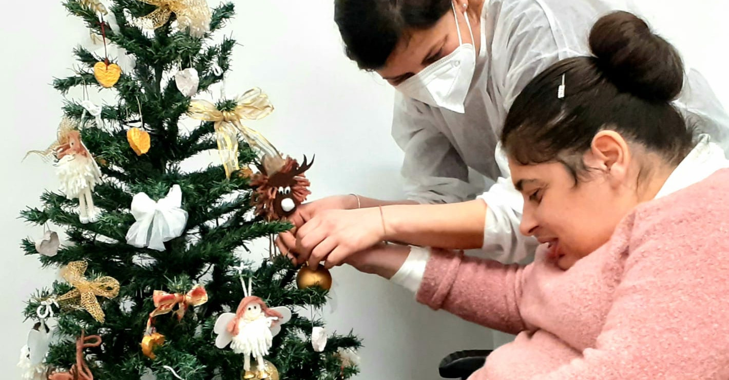 Un'utente del Centro Residenziale di Santo Stefano addobba l'albero di Natale con l'aiuto di un'operatrice.