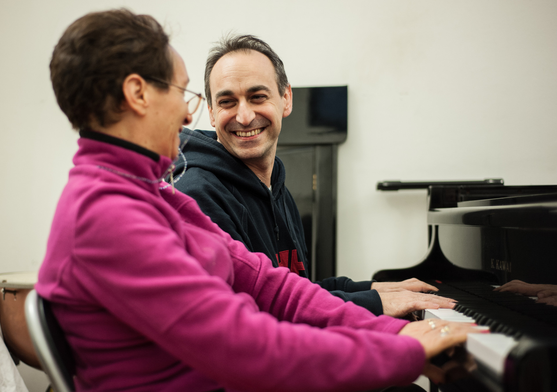 Lorenzo, Musicoterapista presso il Centro di Lesmo, seduto al pianoforte al fianco di una utente adulta. I due si guardano sorridendo sereni