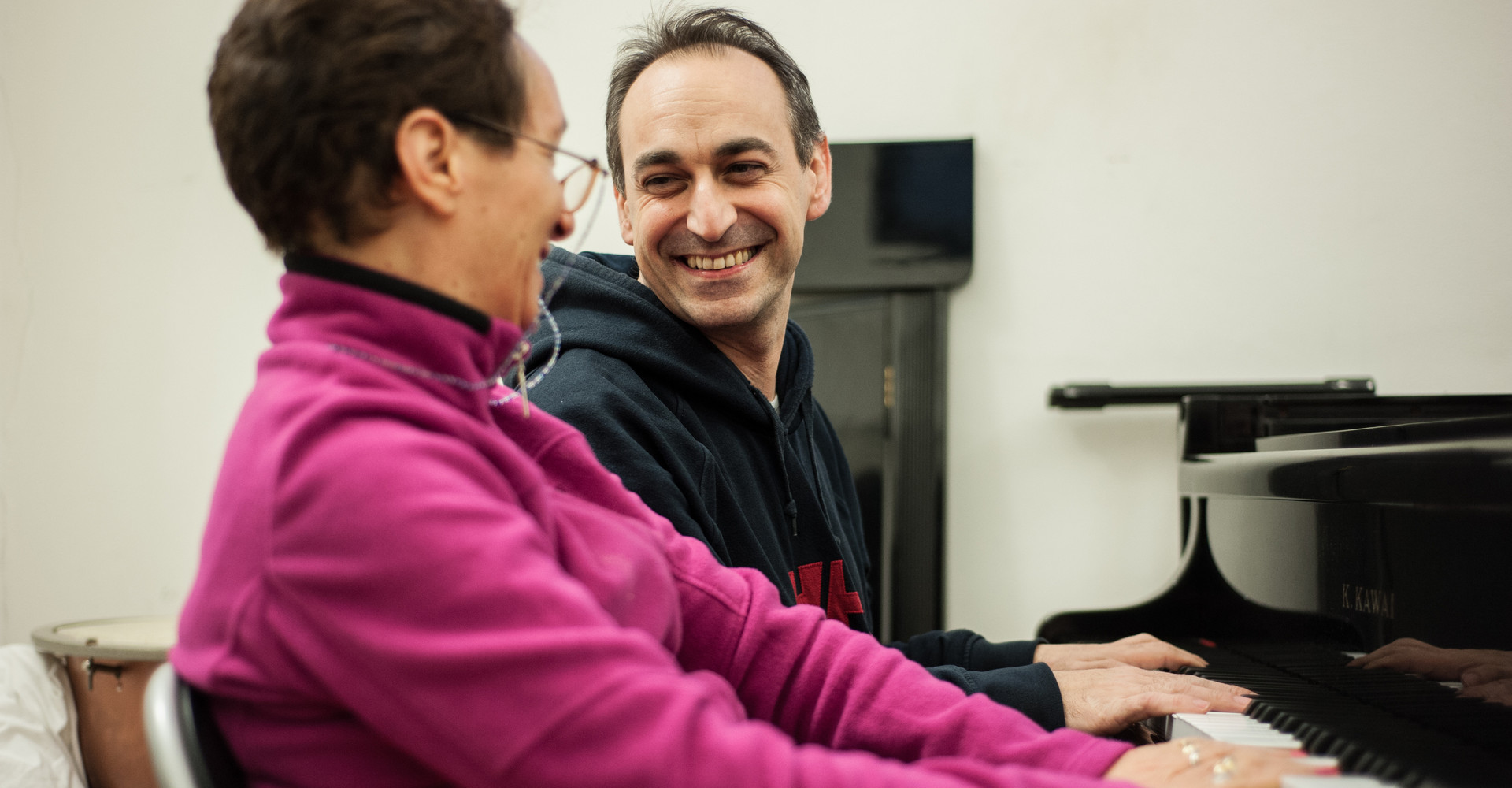 Lorenzo, Musicoterapista presso il Centro di Lesmo, seduto al pianoforte al fianco di una utente adulta. I due si guardano sorridendo sereni