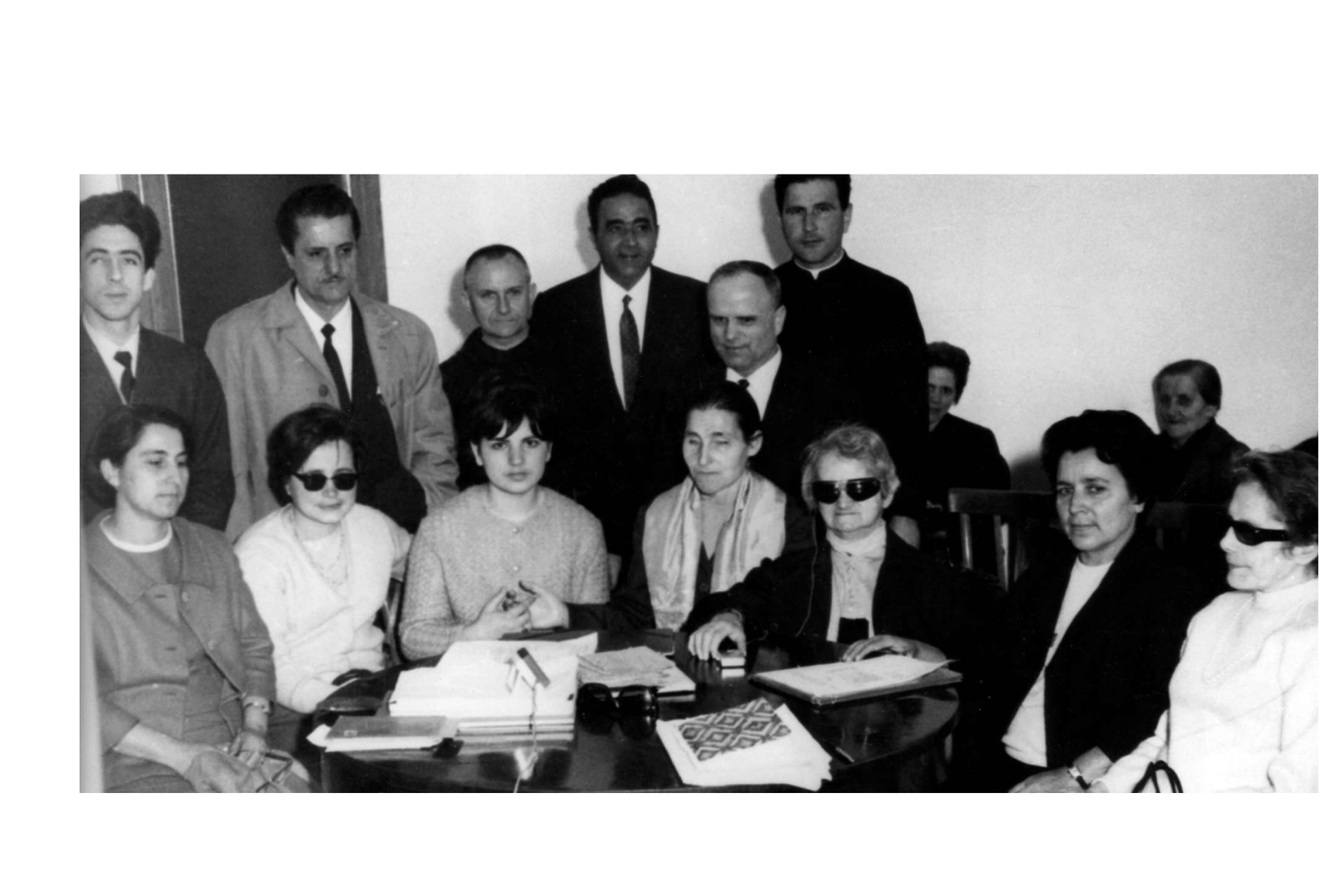 Foto di gruppo dei fondatori della Lega del Filo d'Oro. Sette donne tra cui anche Sabina Santilli, sono sedute attorno ad un tavolo. Dietro di loro sei uomini. L'immagine è in bianco e nero.