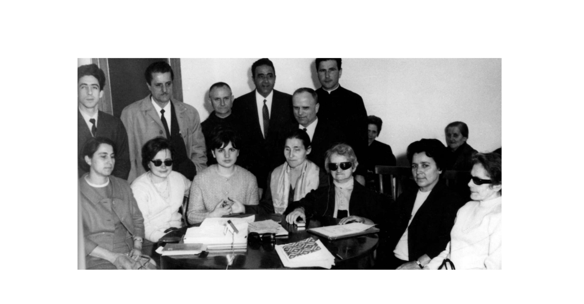 Foto di gruppo dei fondatori della Lega del Filo d'Oro. Sette donne tra cui anche Sabina Santilli, sono sedute attorno ad un tavolo. Dietro di loro sei uomini. L'immagine è in bianco e nero.