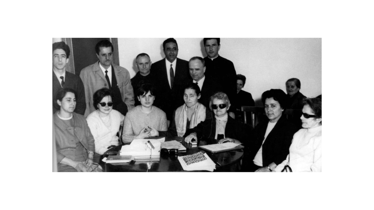 Foto di gruppo dei fondatori della Lega del Filo d'Oro. Sette donne tra cui anche Sabina Santilli, sono sedute attorno ad un tavolo. Dietro di loro sei uomini. L'immagine è in bianco e nero.