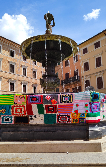 Fontana nella piazza di Osimo decorata con grandi tasselli colorati, tra cui la bandiera italiana, realizzata per lo Yarrn Bombing