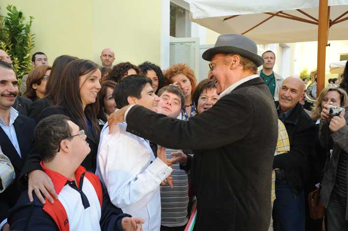 Andrea, utente adulto seguito dalla Lega del Filo d'Oro, felice con Renzo Arbore di profilo insieme a tante persone