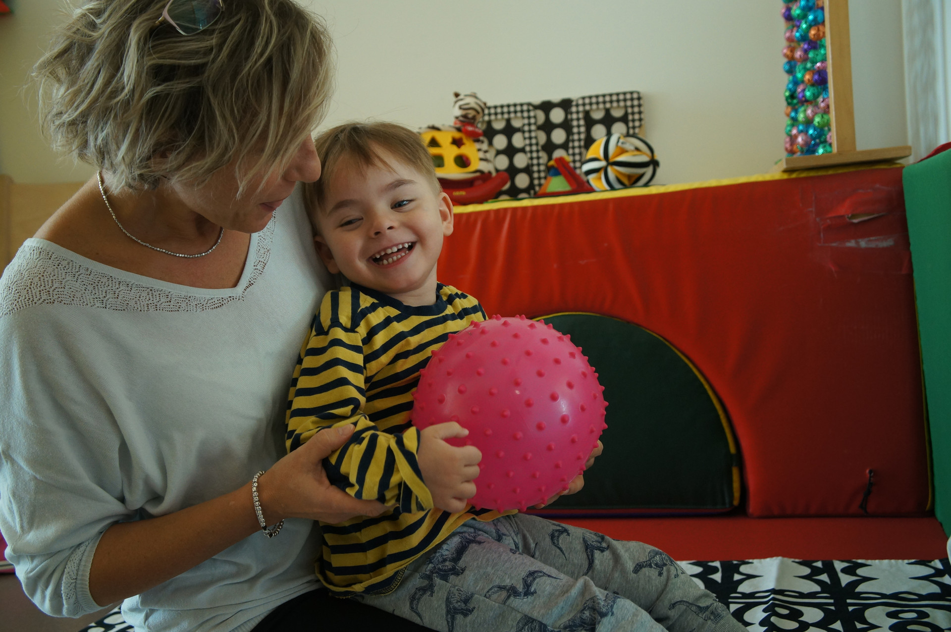 Il piccolo Edoardo, ospite del Centro Diagnostico, è in braccio all'educatrice e ride stringendo una palla di gomma rosa