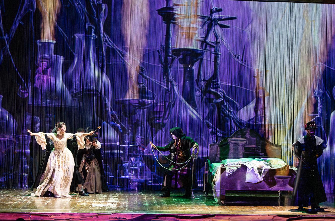 Un'attrice in abito bianco d’epoca, a braccia aperte, domina la scena. Alla sua sinistra, due attori in nero: uno si avvicina con una corda, l’altro osserva immobile il pubblico. Momento intenso dell'opera "Una Missione per Due", la orima opera lirica "fai da te".