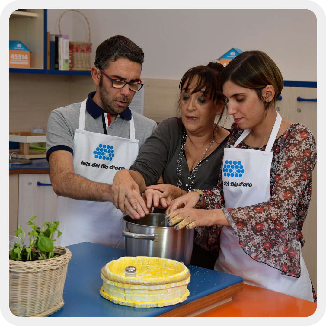 Francesca e Stefano, due giovani con disabilità visive e uditive, preparano una torta nella cucina didattica della Lega del Filo d'Oro con l'aiuto di una loro educatrice.