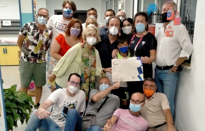 Matilde festeggia l'esperienza di Tokio, tiene in mano una pergamena ed è circondata da un gruppo di amici e operatori. Tutti indossano la mascherina
