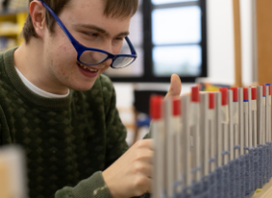 Victor, giovane utente della Lega del Filo d'Oro, lavora con alcuni strumenti per creare un'opera in maglia da usare per lo Yarn Bombing. Mentre lavora sorride divertito.