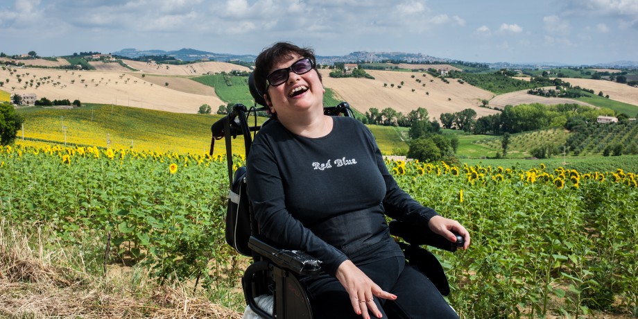 Paola, ospite residenziale del Centro Nazionale di Osimo, in gita sulle colline Marchigiane. Sullo sfondo un campo di girasoli e le colline.