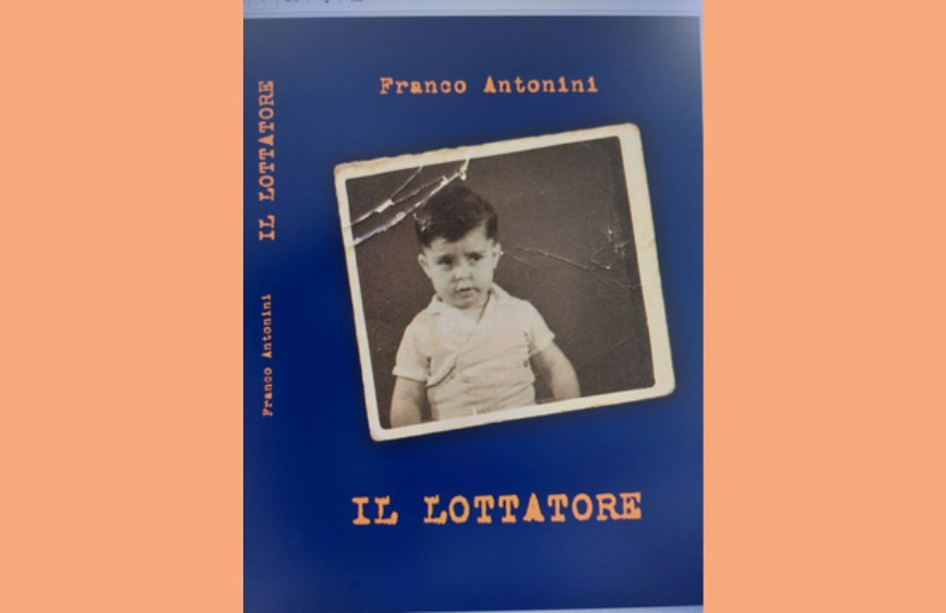 copertina di un libro intitolato "IL LOTTATORE" di Franco Antonini. La copertina è di un blu scuro intenso e presenta al centro una vecchia fotografia in bianco e nero, incorniciata da un bordo bianco che sembra rovinato, con una crepa visibile in alto a sinistra. La foto ritrae un bambino con capelli scuri e uno sguardo serio o forse preoccupato, rivolto verso l'osservatore. Il titolo del libro è scritto in alto e in basso, mentre il nome dell'autore è riportato in alto e verticalmente sul lato sinistro.