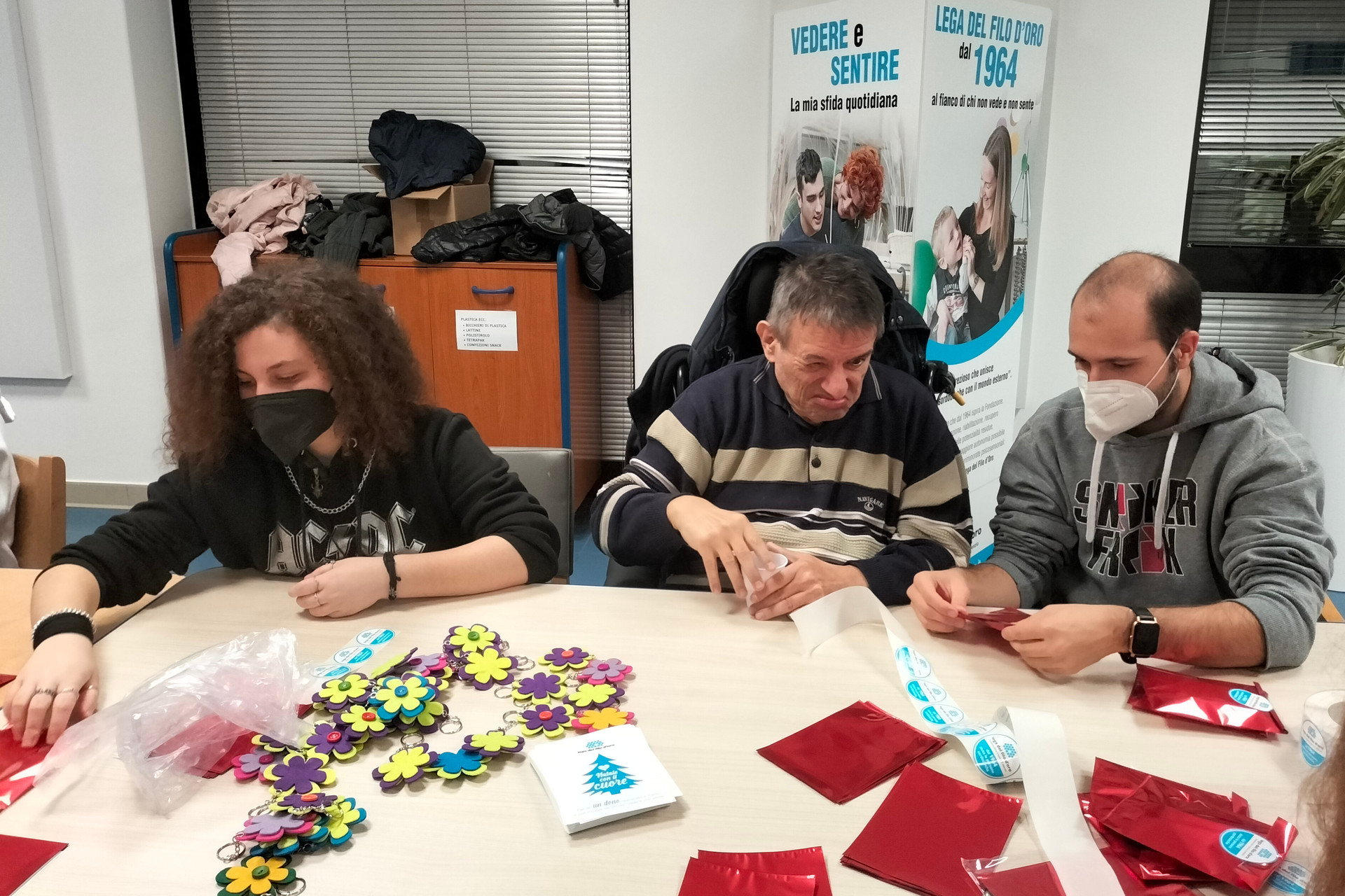 Utente e volontari durante un'attività presso la Lega del Filo d'Oro. Stanno preparando dei pacchetti regalo