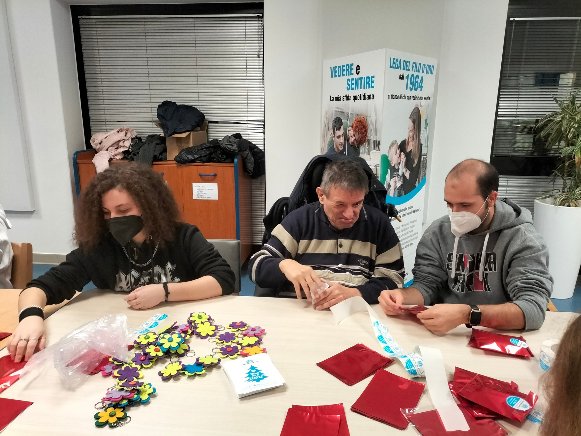 Utente e volontari durante un'attività presso la Lega del Filo d'Oro. Stanno preparando dei pacchetti regalo