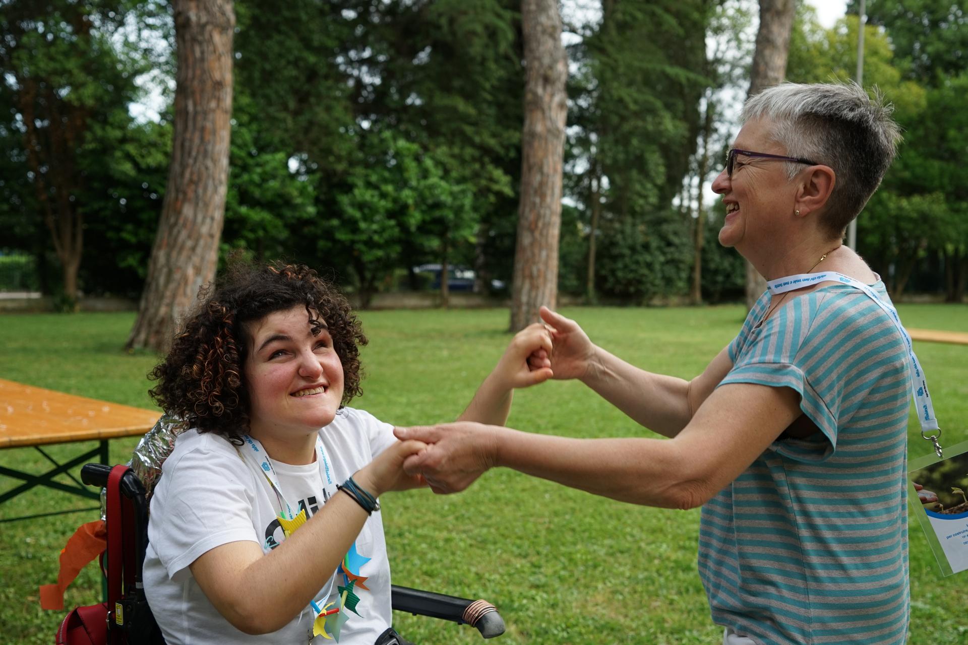 Nel parco dell'hotel Sara, un'utente del Centro di Lesmo in carrozzina si diverte tenendosi per mano con una volontaria della Lega del Filo d'Oro