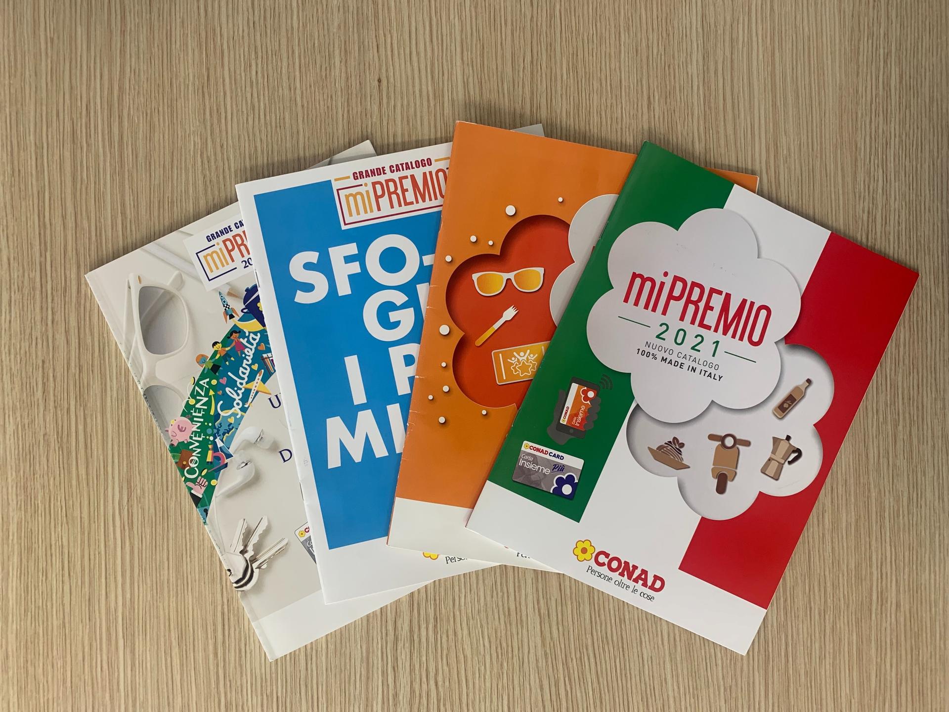 Quattro cataloghi Conad di quattro diversi anni sono appoggiati a ventaglio su una scrivania in legno.