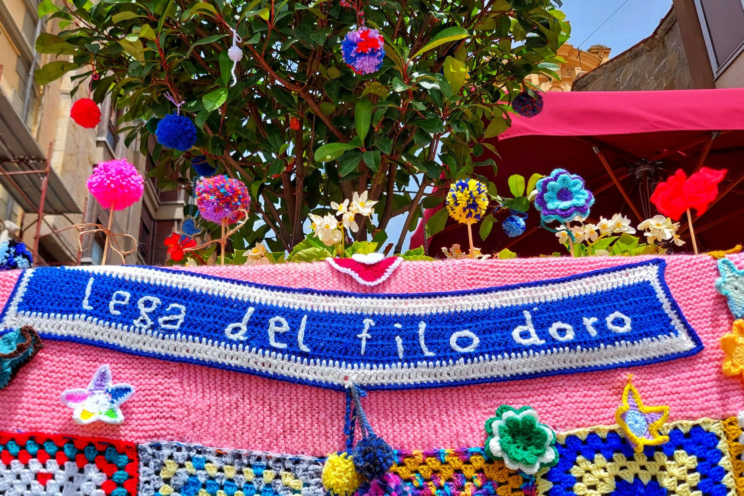 Elementi colorati dello yarn bombing di pisa con la scritta Lega del Filo d'oro in bianco sull'azzurro
