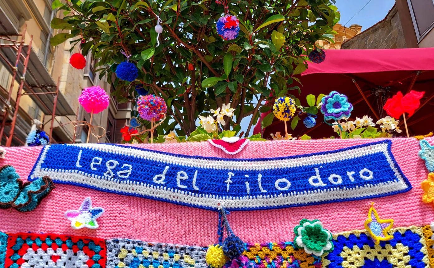Elementi colorati dello yarn bombing di pisa con la scritta Lega del Filo d'oro in bianco sull'azzurro