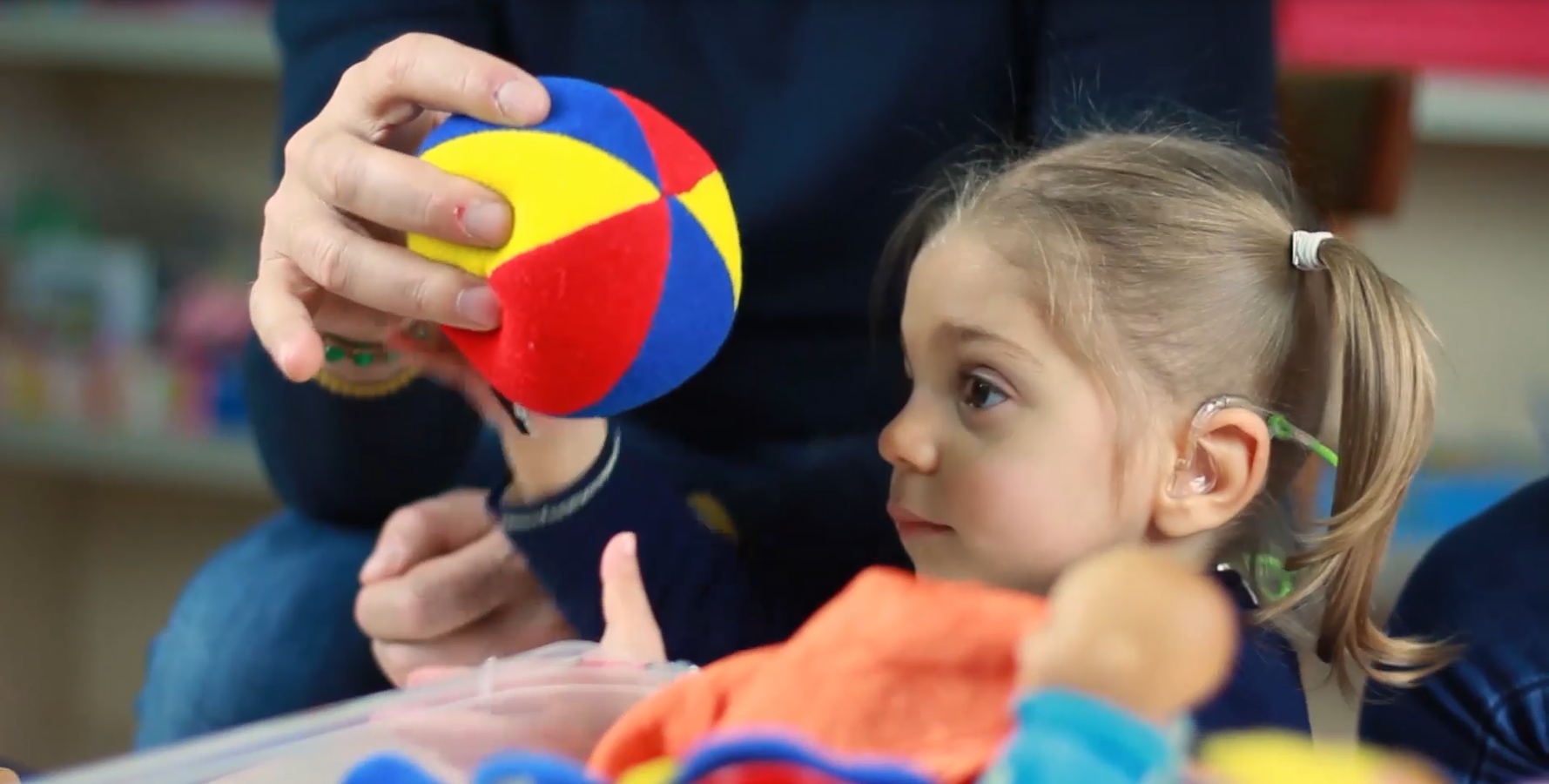 La piccola Sveva, bambina con sindrome di Charge, prende una pallina di stoffa colorata dalle mani del papà