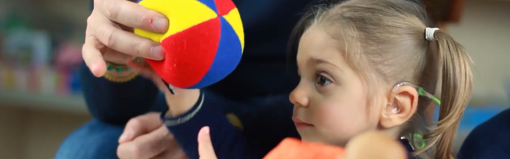 La piccola Sveva, bambina con sindrome di Charge, prende una pallina di stoffa colorata dalle mani del papà