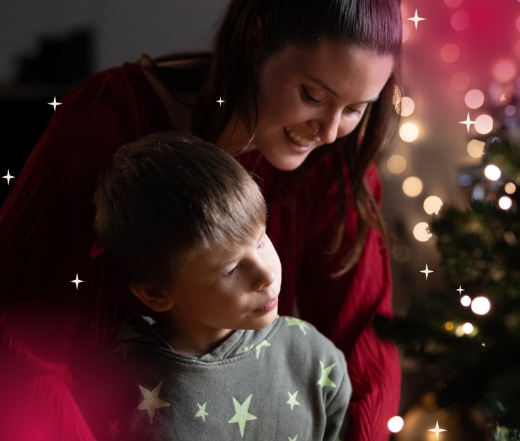 Foto natalizia di Matteo, bambino cieco, insieme alla sua educatrice. Sullo sfondo un albero di Natale illuminato da tante luci colorate. Un momento di affetto e magia durante le festività.