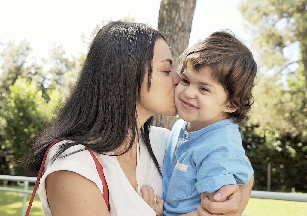 Mamma Samuela tiene in braccio Agostino, bambino con sindrome di Charge, e gli dà un bacio sulla guancia mentre passeggiano per i giardini del Centro di Osimo
