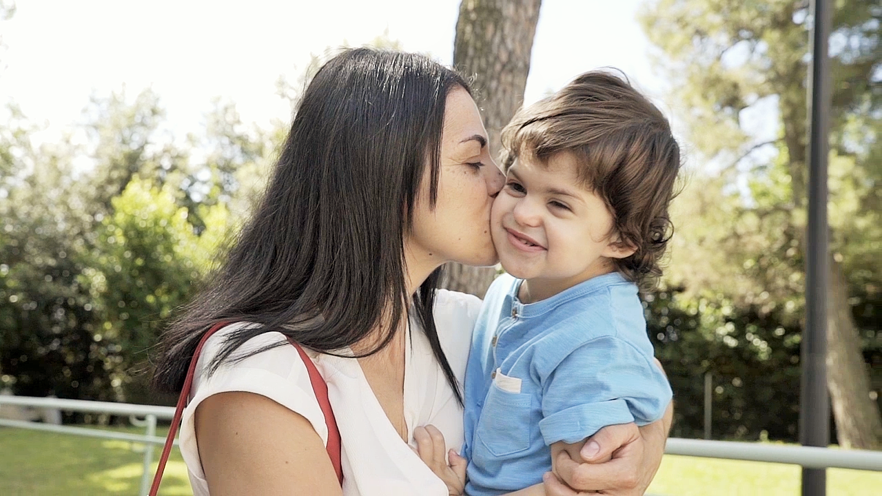 Mamma Samuela tiene in braccio Agostino, bambino con sindrome di Charge, e gli dà un bacio sulla guancia mentre passeggiano per i giardini del Centro di Osimo
