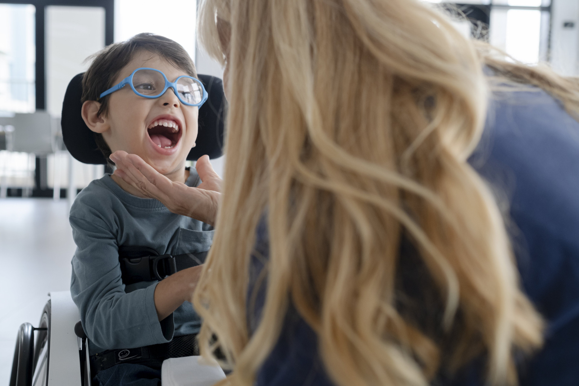 Il piccolo Nicola insieme alla fisioterapista della Lega del Filo d'Oro in un momento di pausa delle riprese di campagna. La fisioterapista accarezza il viso di Nicola e lui esplode in una risata.