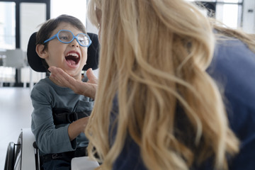 Il piccolo Nicola insieme alla fisioterapista della Lega del Filo d'Oro in un momento di pausa delle riprese di campagna. La fisioterapista accarezza il viso di Nicola e lui esplode in una risata.