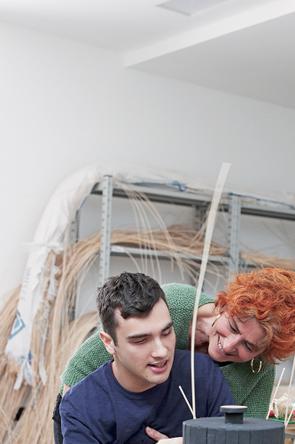 Un utente adulto della Lega del Filo d'Oro, intento a costruire un cestino di midollino con l'aiuto di un'operatrice. 