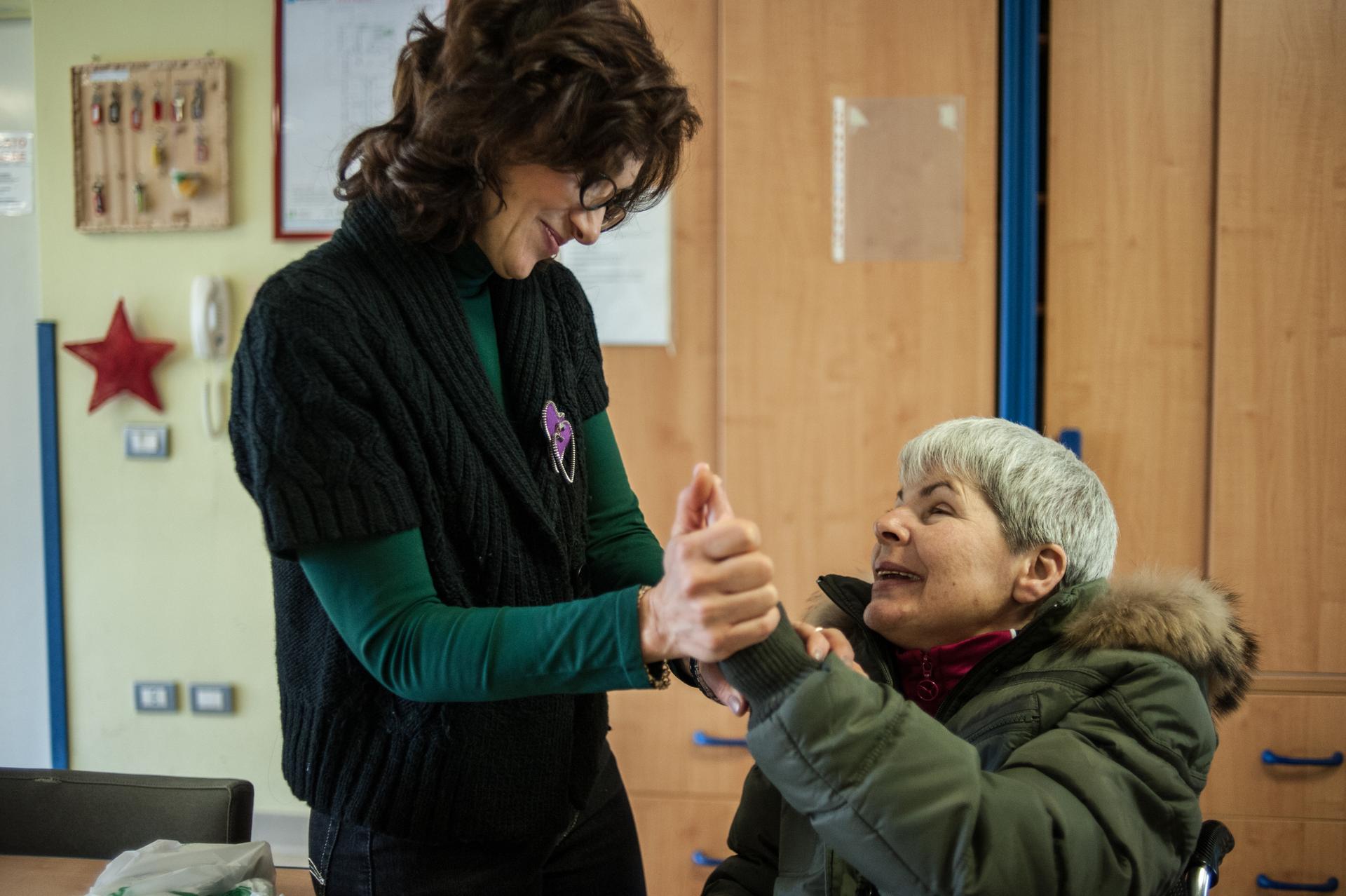 Un’educatrice della Lega del Filo d'Oro stringe con dolcezza la mano di un’utente seduta di fronte a lei. Un gesto silenzioso ma profondo, che racconta fiducia, ascolto e vicinanza.