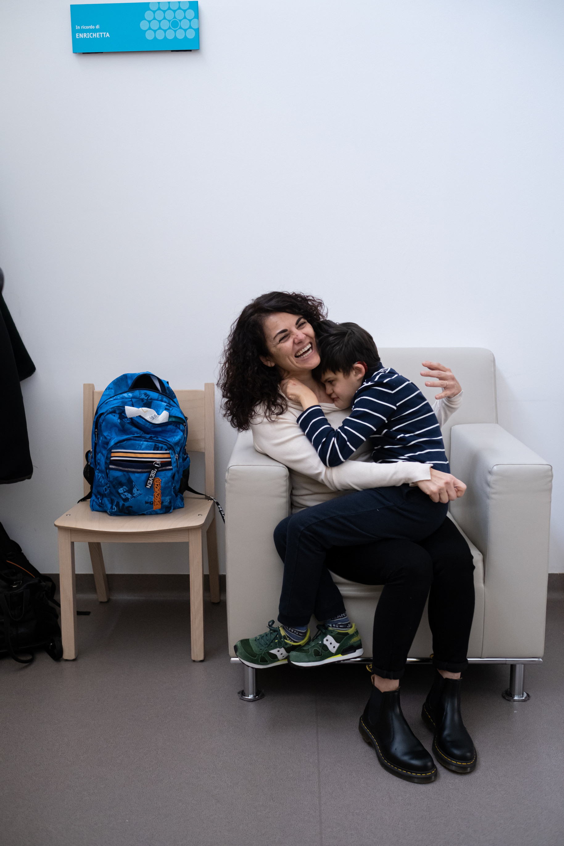 Agostino, ragazzo seguito dalla Lega del Filo d'Oro, è seduto sulle gambe di sua madre Samuela, che sorride, e la abbraccia. Entrambi si trovano su una poltrona bianca al Centro di Osimo