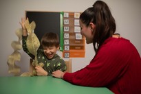 Matteo, bambino non vedente e con deficit cognitivo, ride di gusto scoprendo con il tatto una grande ghirlanda natalizia, sotto lo sguardo divertito della sua educatrice. Si trovano in un'aula del Centro di Osimo