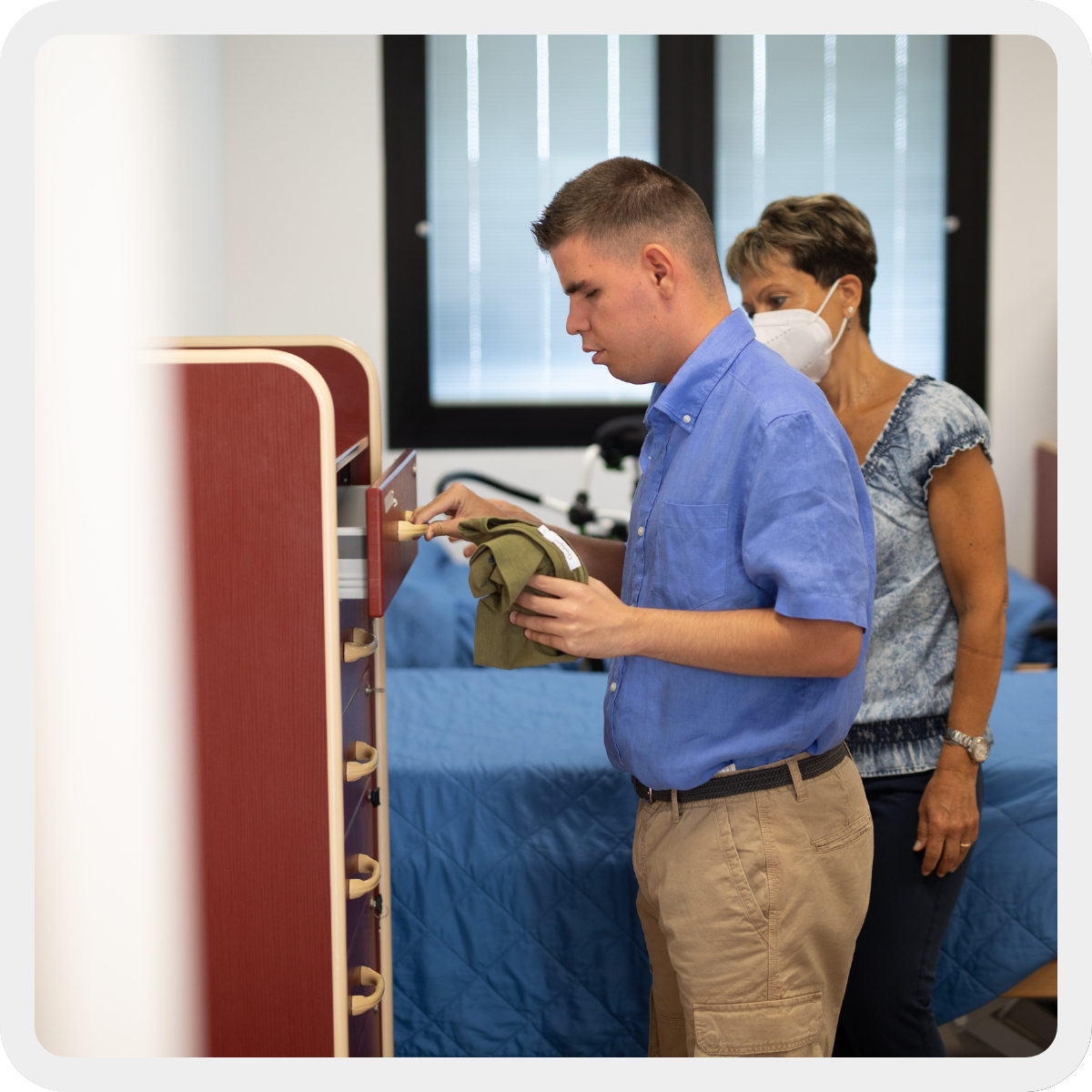 Benedetto, persona con pluridisabilità, sistema i suoi vestiti nella cassettiera aiutato dalla sua educatrice Sonia. 