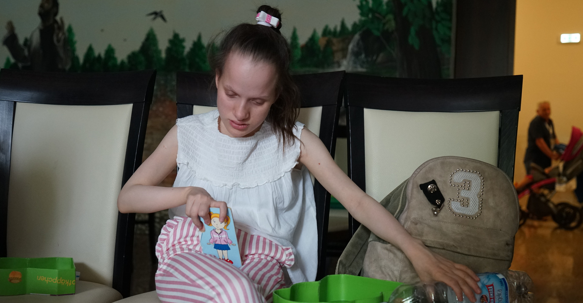 Ragazza sordocieca seduta in una stanza laboratorio, tiene in mano un cartoncino con un disegno e una bottiglia di plastica. Lo sguardo è rivolto verso il basso.