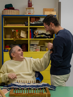 Un utente adulo della Lega del Filo d'Oro, insieme a un volontario, nel laboratorio, che scherzano insieme