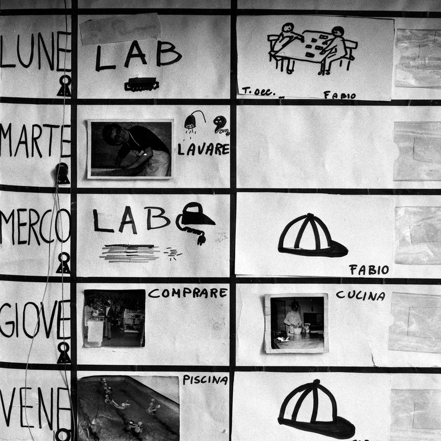 In bianco e nero, la foto ritrae un calendario pittografico, con una tabella in cui sono segnati i giorni della settimana, le attività e gli incaricati di queste.