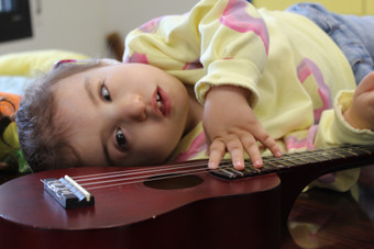 Primo piano di Sophie, bimba sordocieca, che tocca le corde di una piccola chitarra. Sophie è distesa, indossa una maglietta gialla a fantasia 