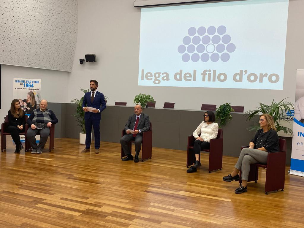 Il presidente Rossano Bartoli ed altri ospiti presenziano in occasione della giornata del sostenitore. Sullo sfondo è proiettato il logo della Fondazione. 